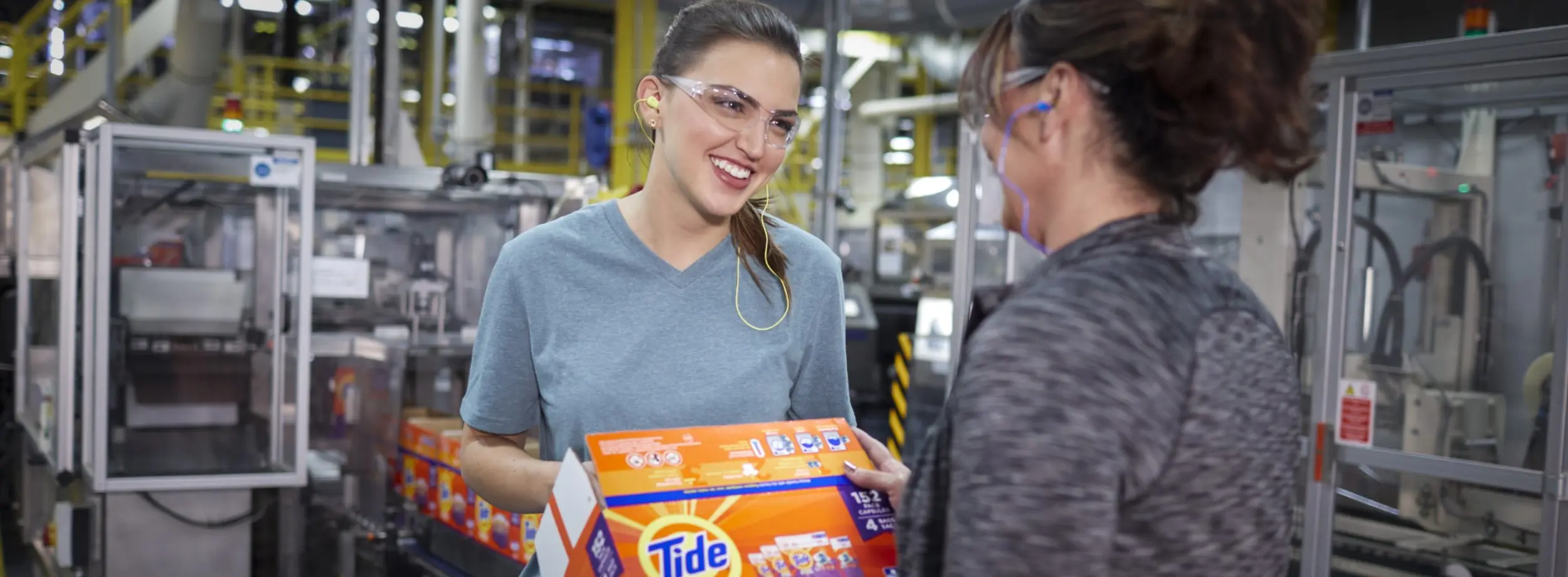 P&G employee hands box of Tide PODS to another P&G employee whose back is to the camera. 