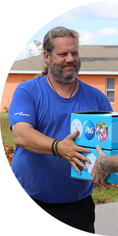 A man with a beard smiling and handing P&G branded boxes to someone in need.